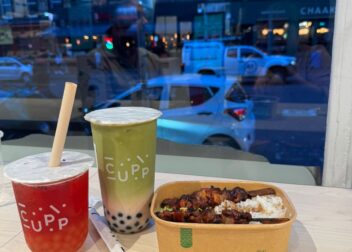Two bubble teas from CUPP and a rice-and-skewers meal in a compostable Vegware container, placed on a table inside a café with a view of a busy Edinburgh street.