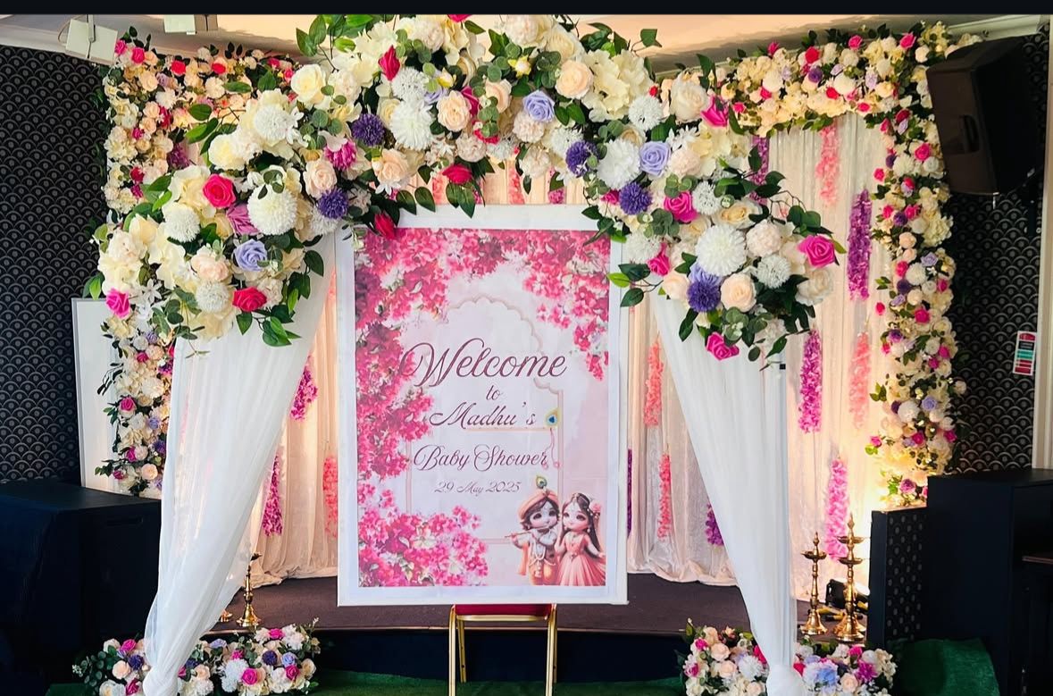 Floral baby shower welcome arch with pink and purple flowers and a welcome board for "Madhu's Baby Shower