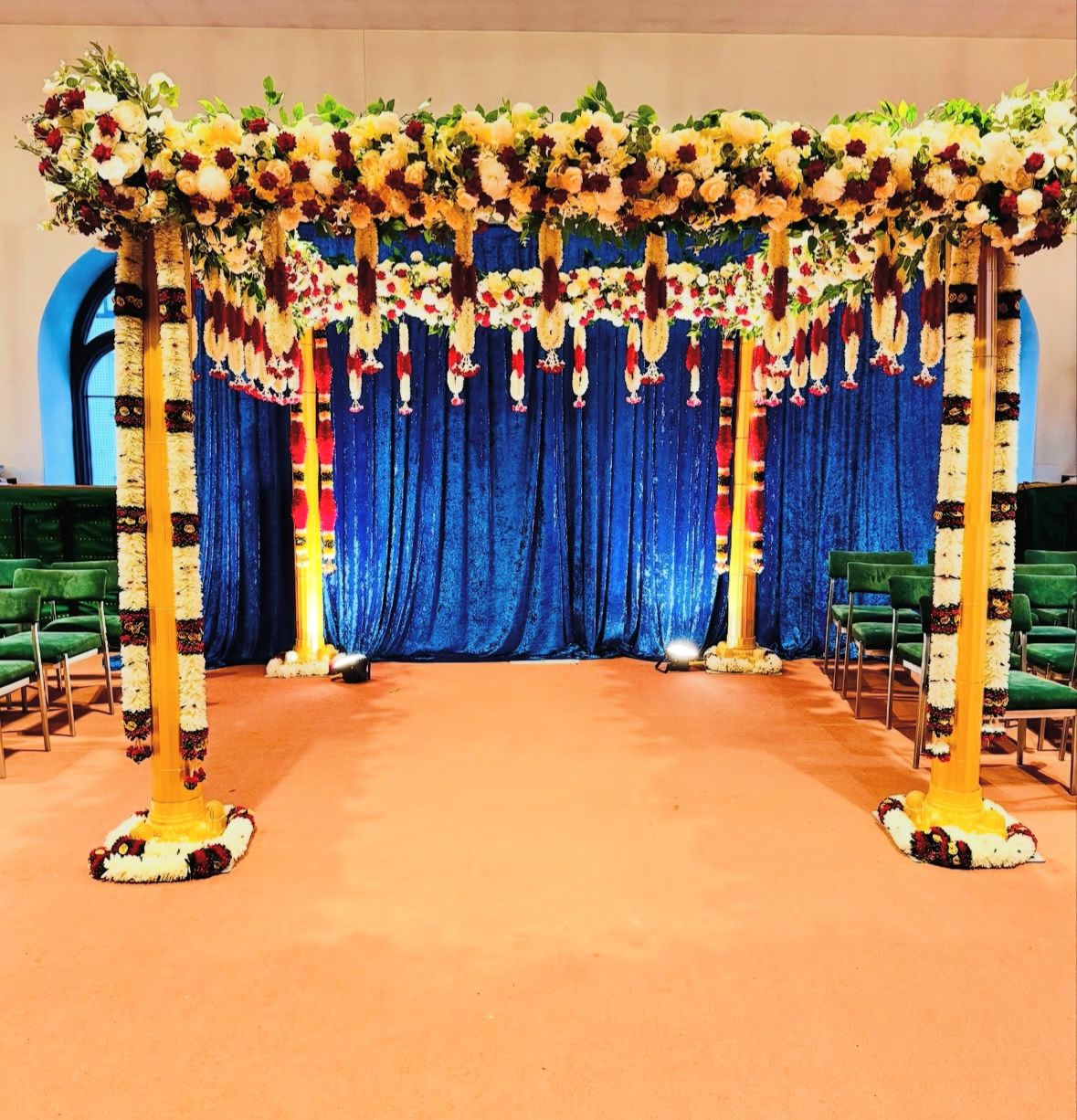 Traditional Indian mandap decorated with marigolds and fresh flower garlands in front of blue velvet backdrop