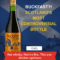 A bottle of Buckfast tonic wine placed against the backdrop of a Scottish flag and Edinburgh Castle. Bold yellow and white text reads: “BUCKFAST?! SCOTLAND'S MOST CONTROVERSIAL BOTTLE.” A red banner below states: Not whisky. Not Irn-Bru. This one divides opinions.